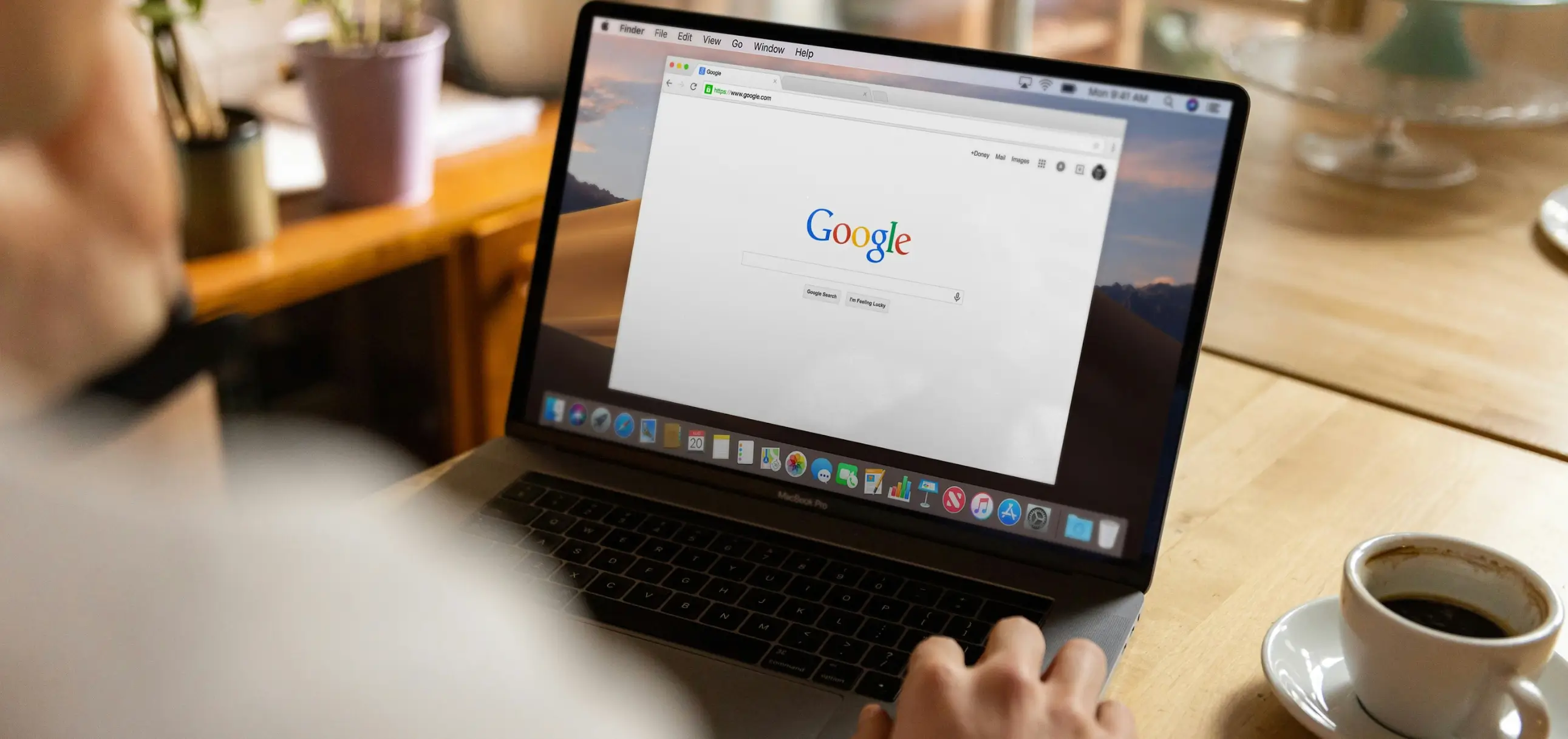 Person using a laptop showing the Google homepage, with a cup of coffee on the table
