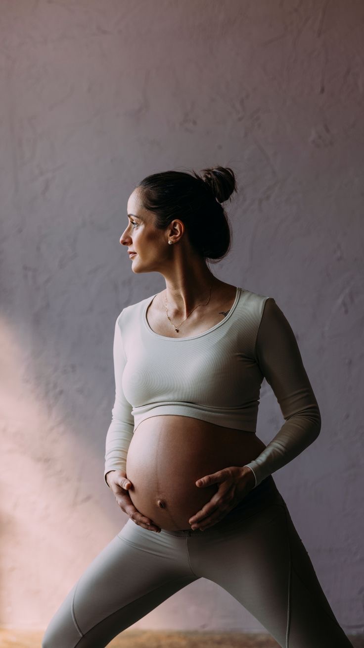 Gravid kvinde i rolig traeningsposition med haenderne på maven, varmt naturligt lys