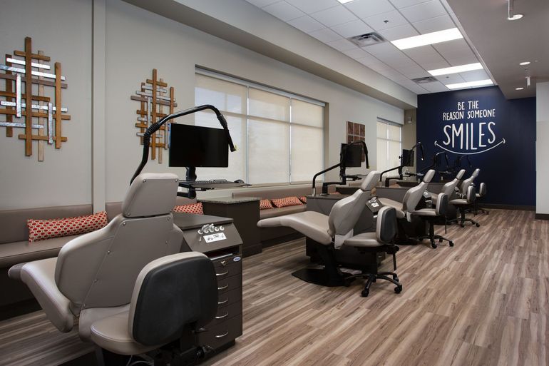 Modern, open-concept orthodontic office with rows of reclining patient chairs, monitors, and light wood flooring.