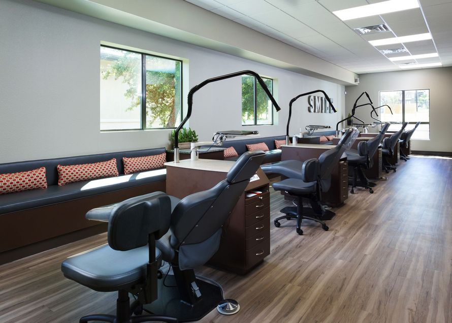 A bright orthodontic office with a long row of dark grey treatment chairs and matching seating along the wall.