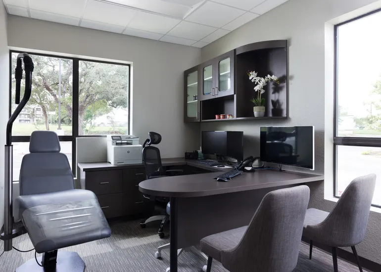 A modern orthodontic consultation office with a desk, monitors, and large windows.
