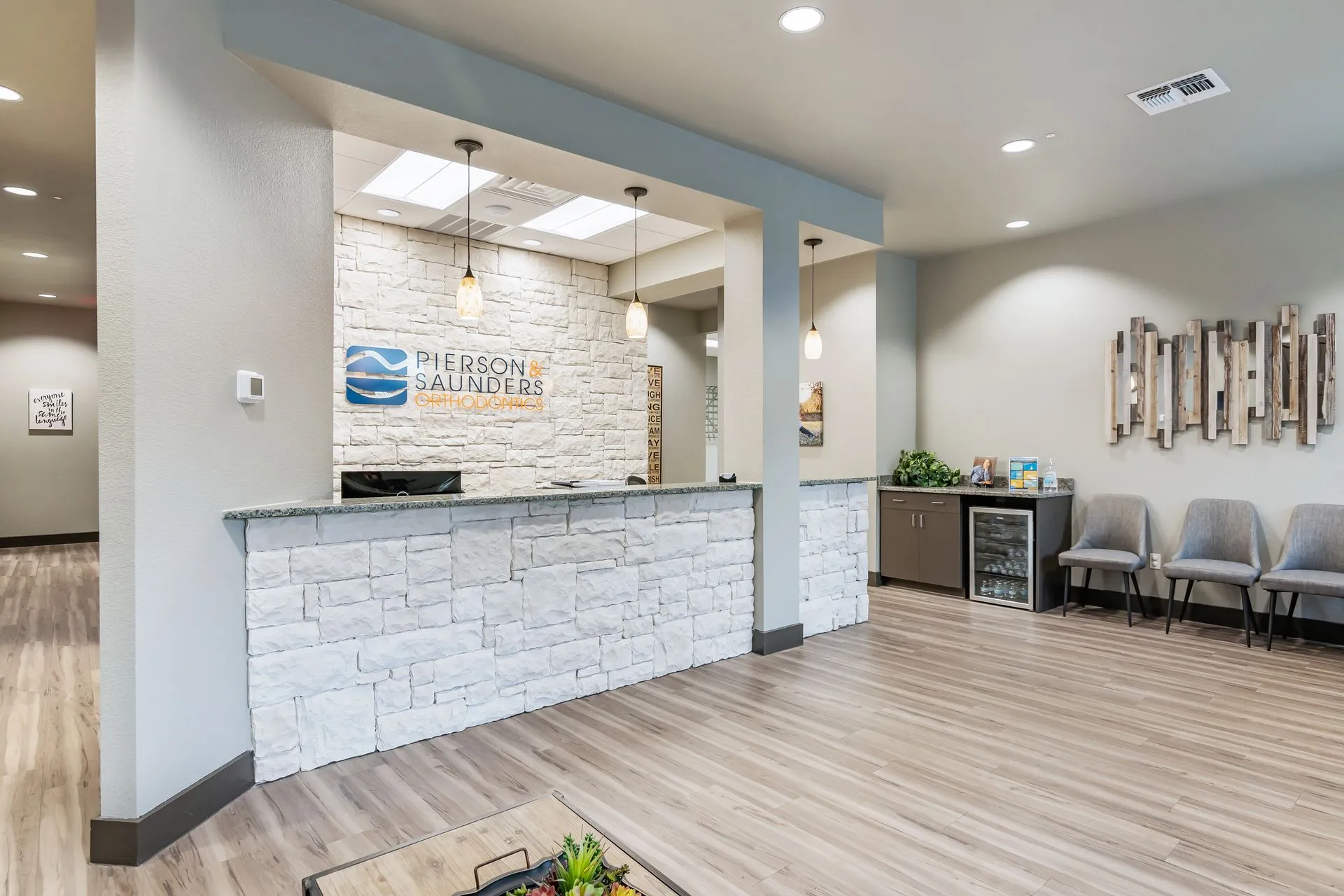 Pierson & Saunders Orthodontics reception area with a white stone wall and the logo.