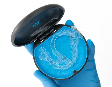 Gloved hands holding Invisalign clear aligners in their case