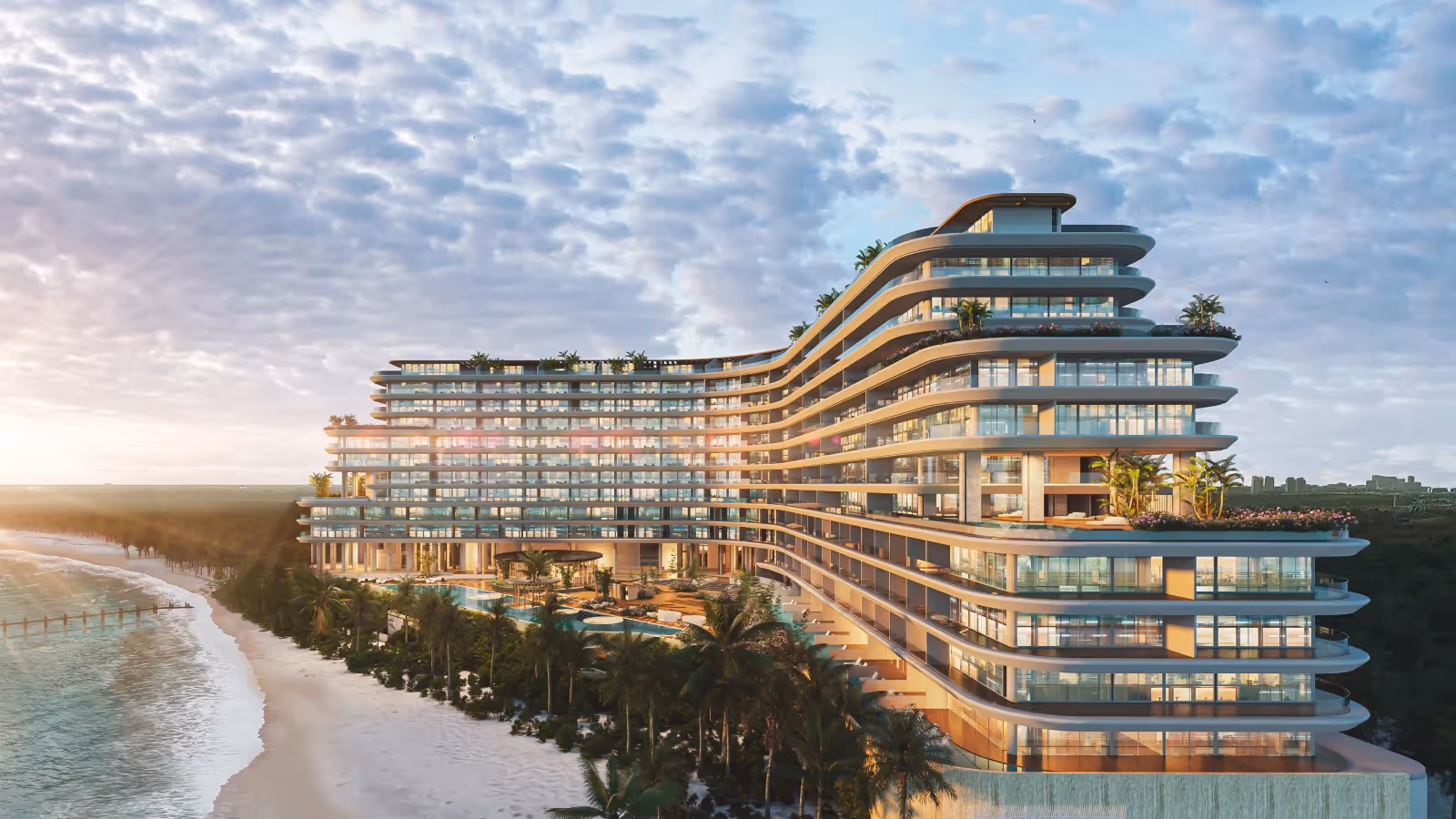 Modern beachfront resort building with curved balconies surrounded by palm trees at sunset.