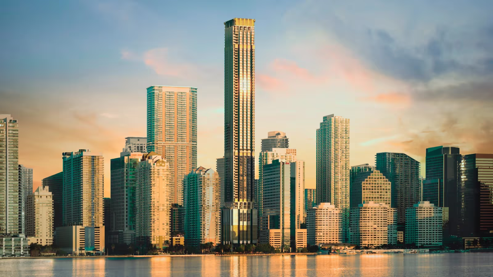 City skyline with modern high-rise buildings reflecting sunlight during sunset over calm water.