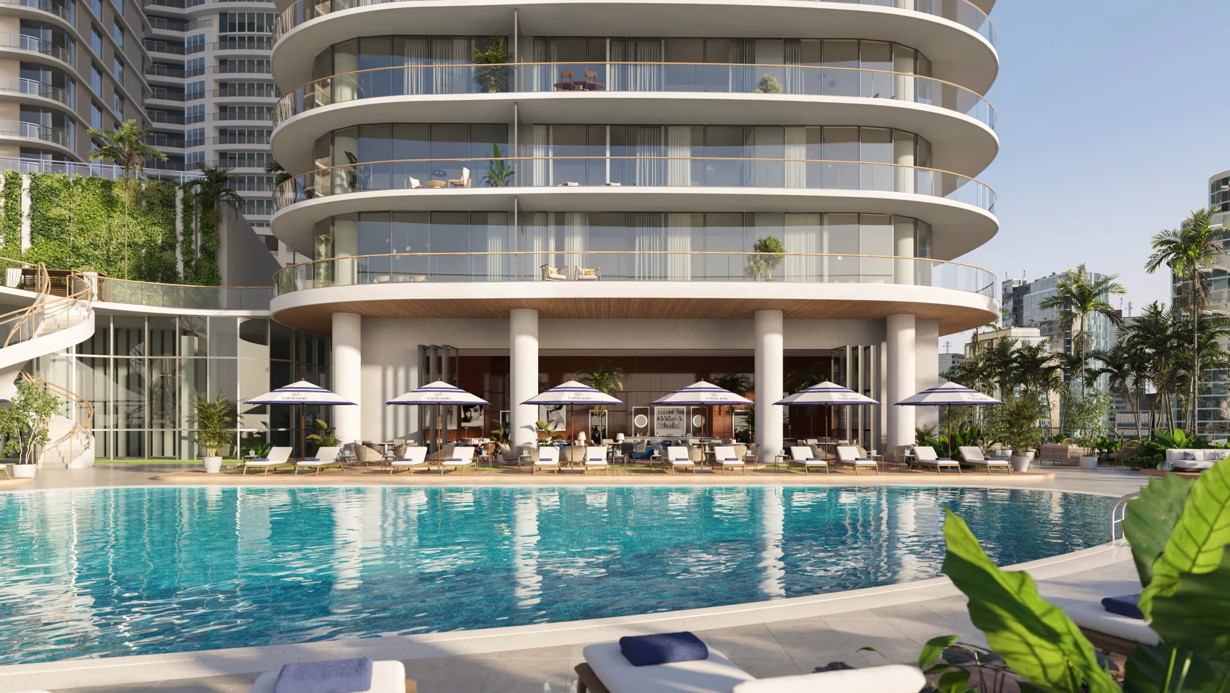 Modern curved building with large balconies overlooks a swimming pool with lounge chairs and umbrellas.