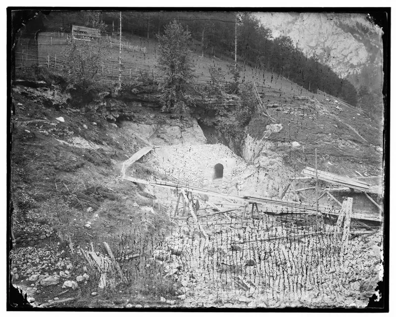 Fotografie um 1870: Baustelle der Quellenleitung in Kaiserbrunn, ein gemauerter Stolleneingang im Hang, davor Geröll und ein Zaun aus Pflöcken