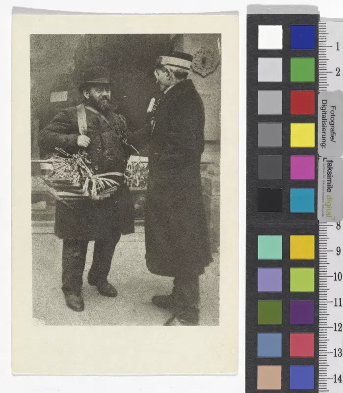 Fotografie um 1908: ein Mann mit Bart und Melone trägt einen Bauchladen und spricht mit einem Dienstmann in Kappe und langem Mantel vor einem Hauseingang