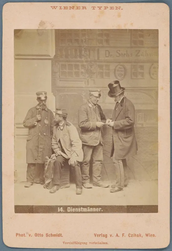 Fotografie: vier Männer vor einer Hausfassade, drei in Mützen, einer mit Zylinder, einer sitzt, zwei reichen sich etwas, unten 14. Dienstmänner