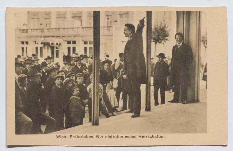 Ansichtskarte um 1908: ein Ausrufer steht erhöht vor einer Bude und zeigt mit erhobenem Arm nach oben, vor ihm eine Menge mit Hüten und Kappen