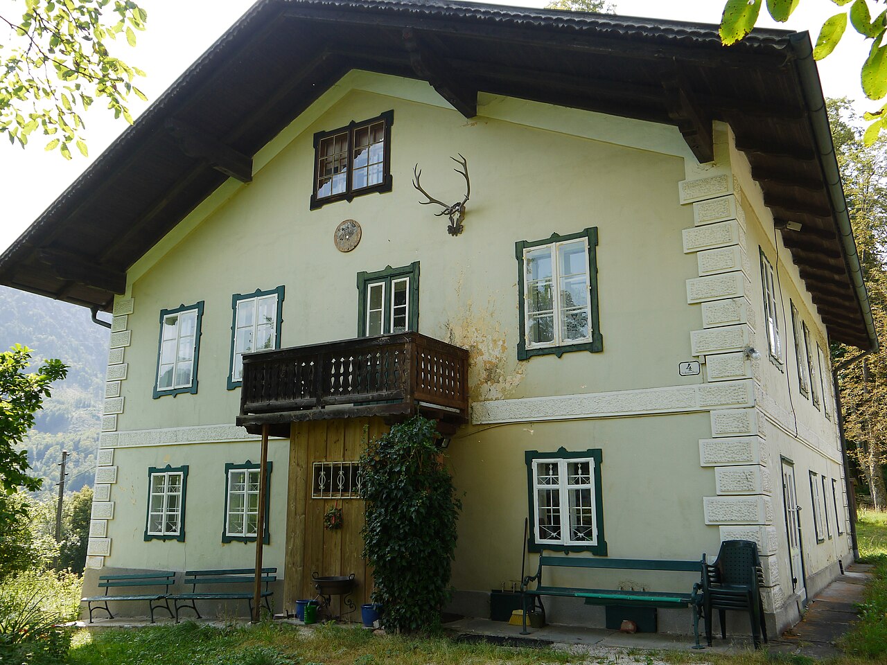 Zweistöckiges Landhaus mit Holzbalkon und grünen Fensterläden, an der Fassade ein Hirschgeweih.