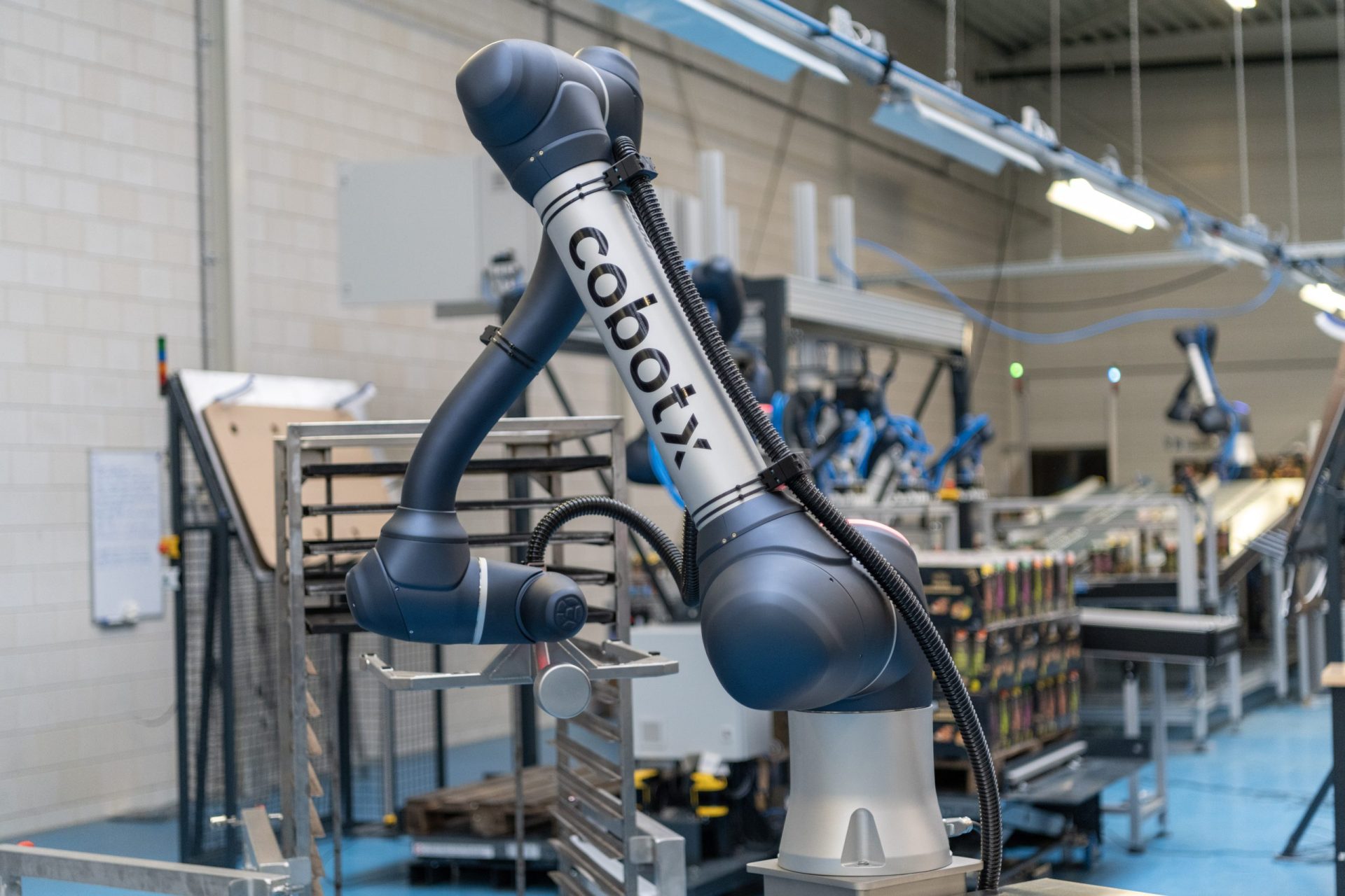 Een industriële robotarm met het label 'cobotix' in een fabriekshal, omgeven door machines en productierekken.