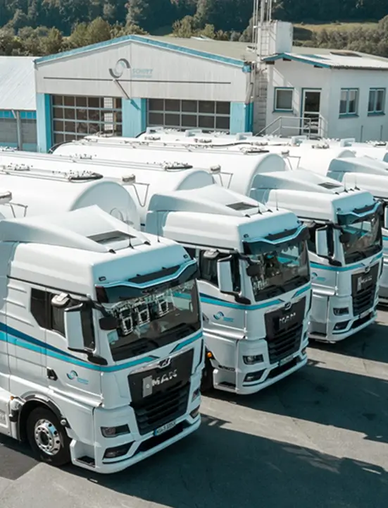 Mehrere weiße Lkw mit blauen Streifen stehen nebeneinander vor einem Gebäude mit dem Schriftzug 'Schott Spedition'.