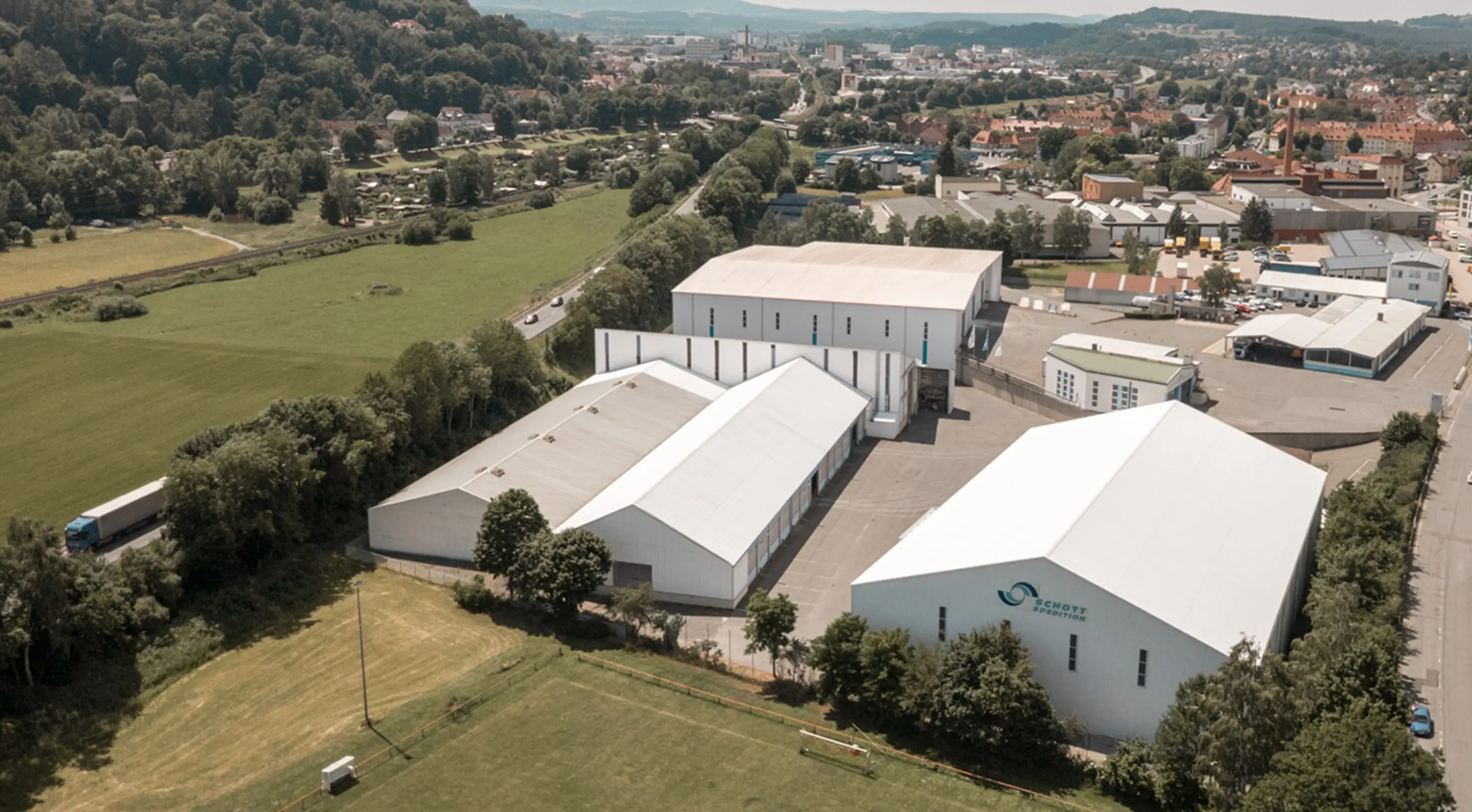 Luftaufnahme des Schott Spedition Standorts mit mehreren großen Lagerhallen und angrenzenden Straßen in Kulmbach.