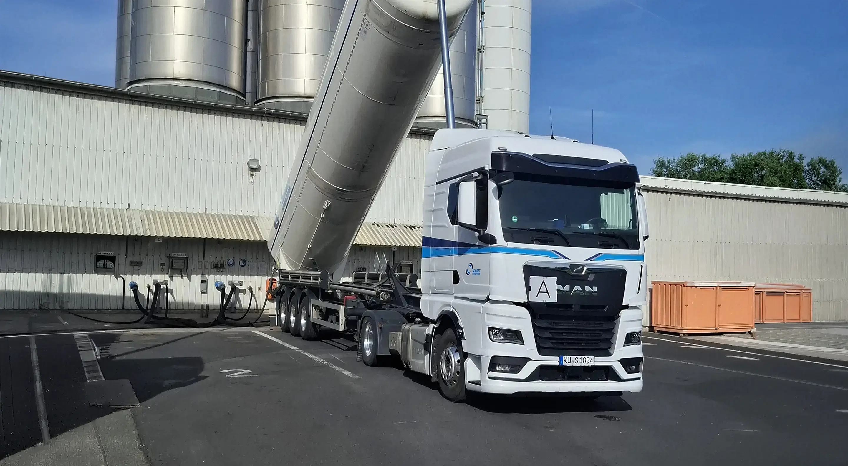 Sattelzugmaschine mit gekipptem Silo-Auflieger der Schott Spedition vor Industriegebäude mit Silos.