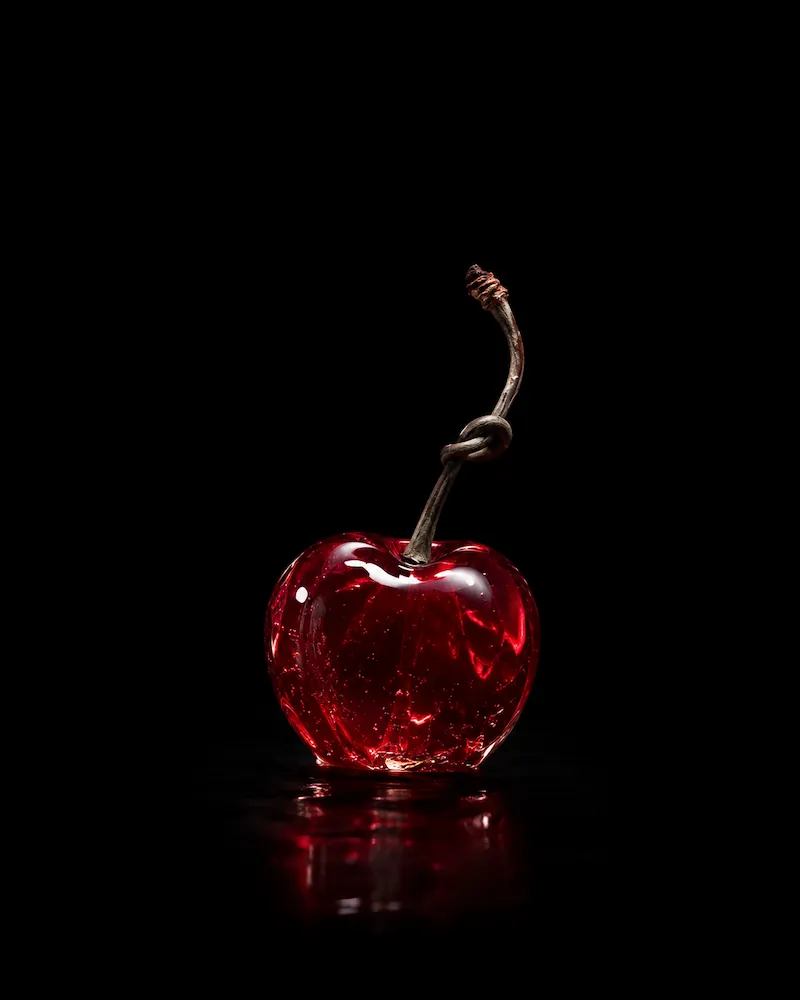 A single glossy red cherry with a knotted stem against a black background, reflecting light and showing internal texture.