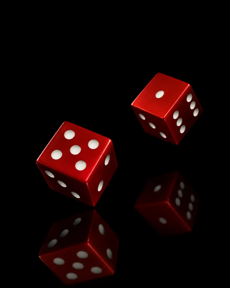 Two red dice with white dots on a reflective black surface, showing six and one on the top faces.