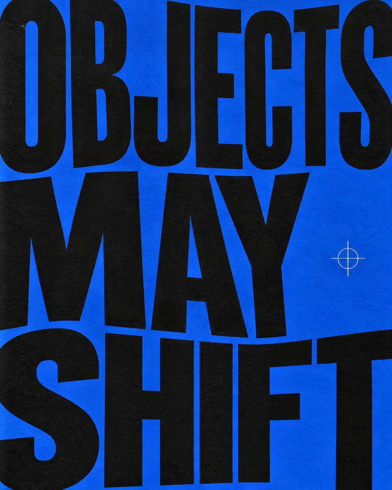Bold black text on a blue background reading 'OBJECTS MAY SHIFT' with a small white crosshair symbol to the right.