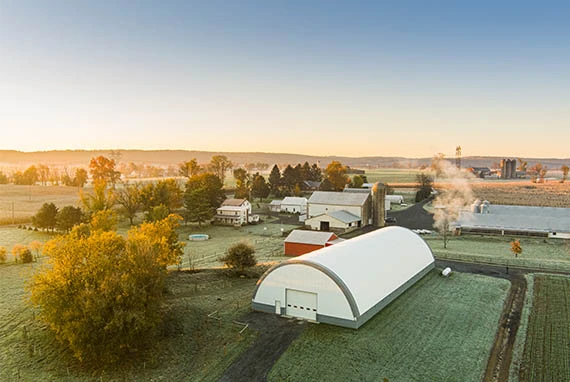 Aerial view of a rural farm with a large white barn, several smaller buildings, trees, and fields.