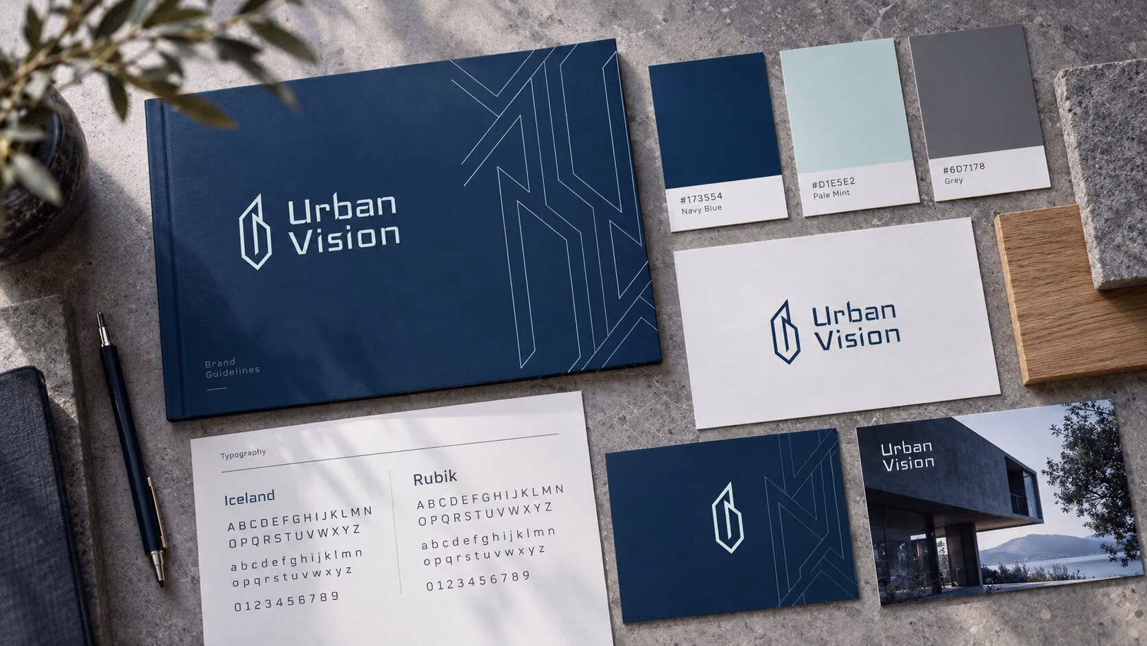 Brand identity palette for Urban Vision showing a navy blue book with logo, colour swatches labeled Navy Blue, Pale Mint, Grey, typography samples for Iceland and Rubik fonts, business cards, a pen, wood and stone textures.