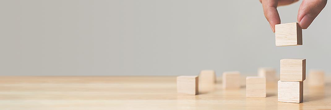 Hand setzt einen Holzwürfel auf eine aufsteigende Treppe aus Würfeln