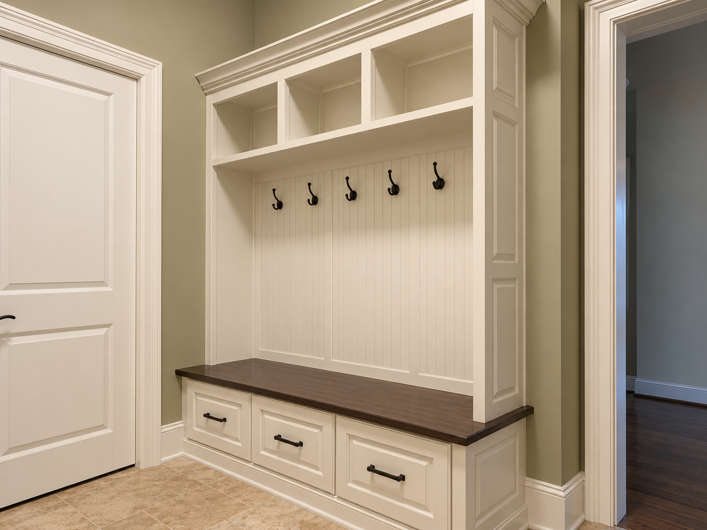Cream mudroom built-in with open cubbies, beadboard back panel, coat hooks, storage drawers and a dark wood bench