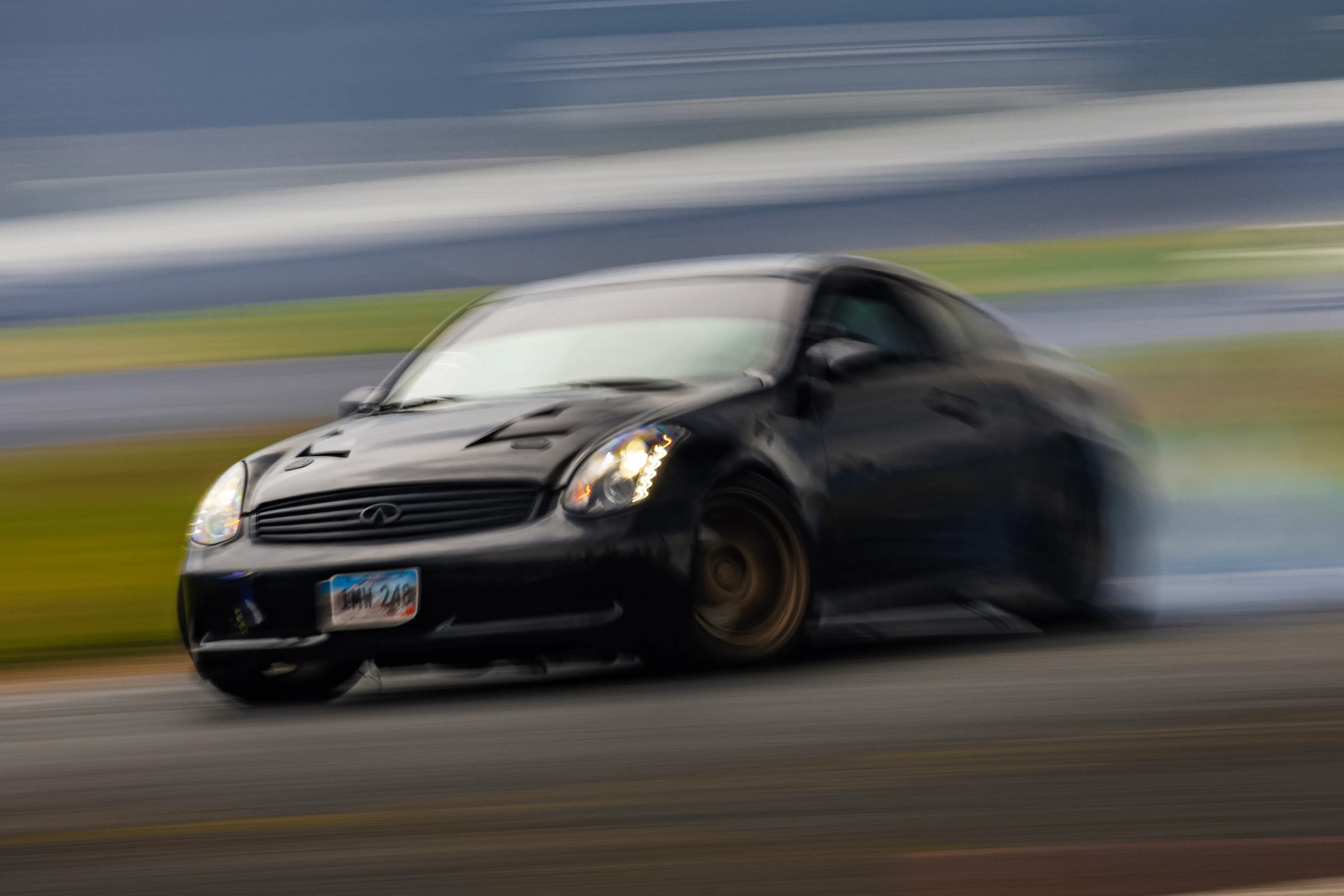 Black Infiniti car drifting on a race track, showing motion blur and smoke from the rear tires.