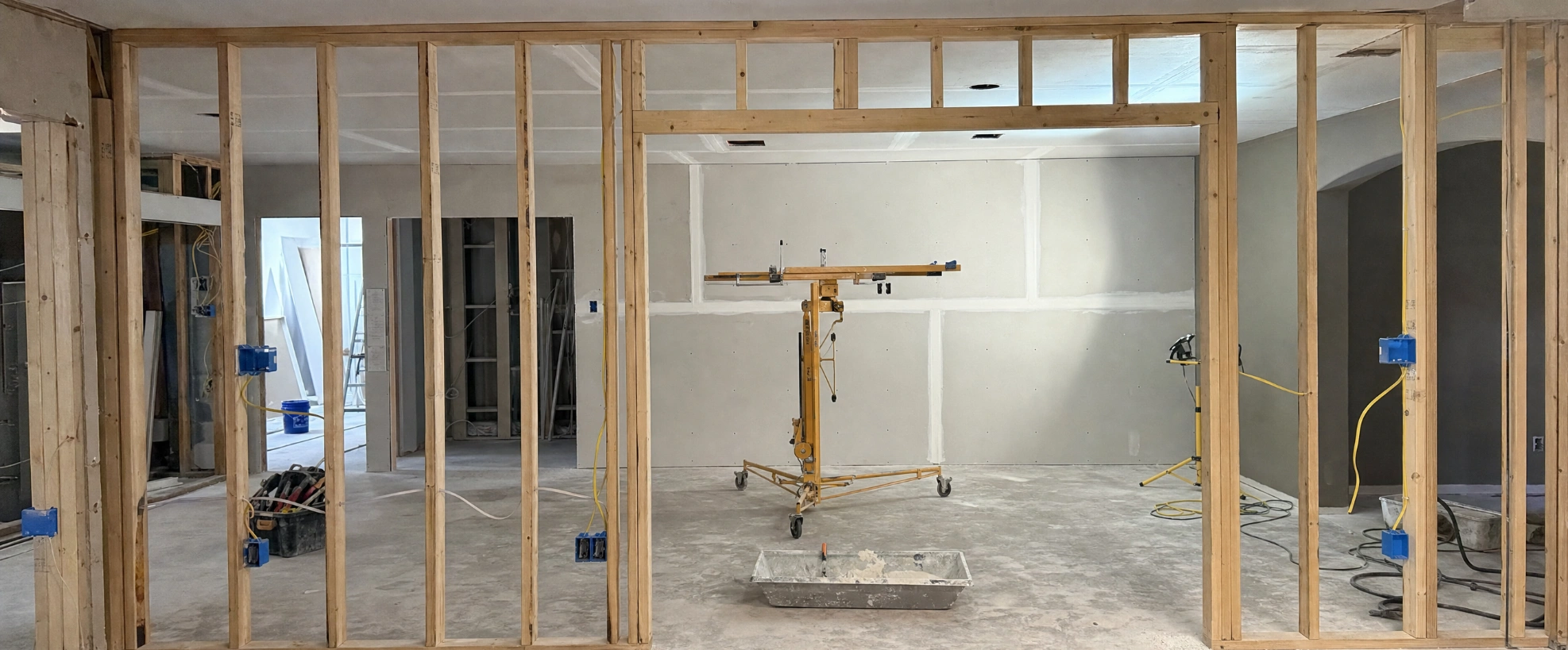 Interior remodel in progress showing new stud framing, electrical rough-in and freshly hung drywall with taped seams
