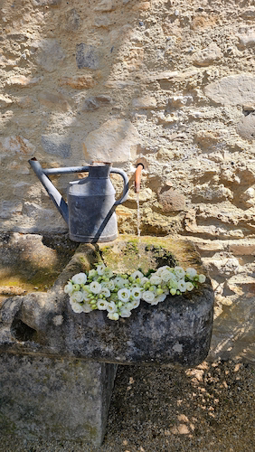 Stone garden fountain with flowers beside a rustic wall