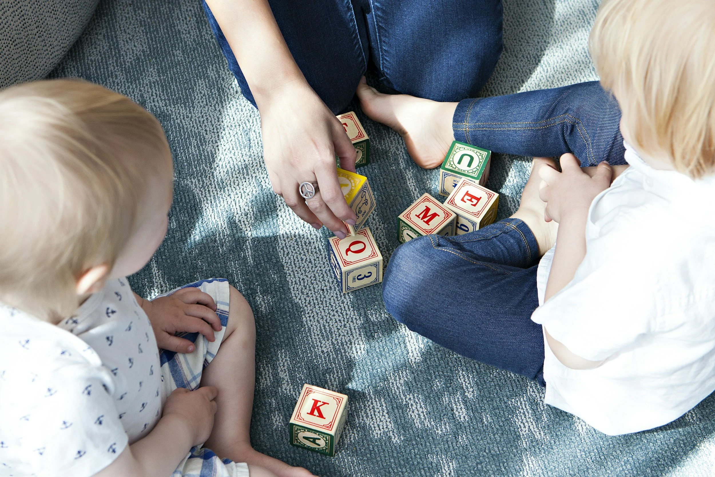 Toddler and adults sitting on a rug playing with alphabet letter blocks
