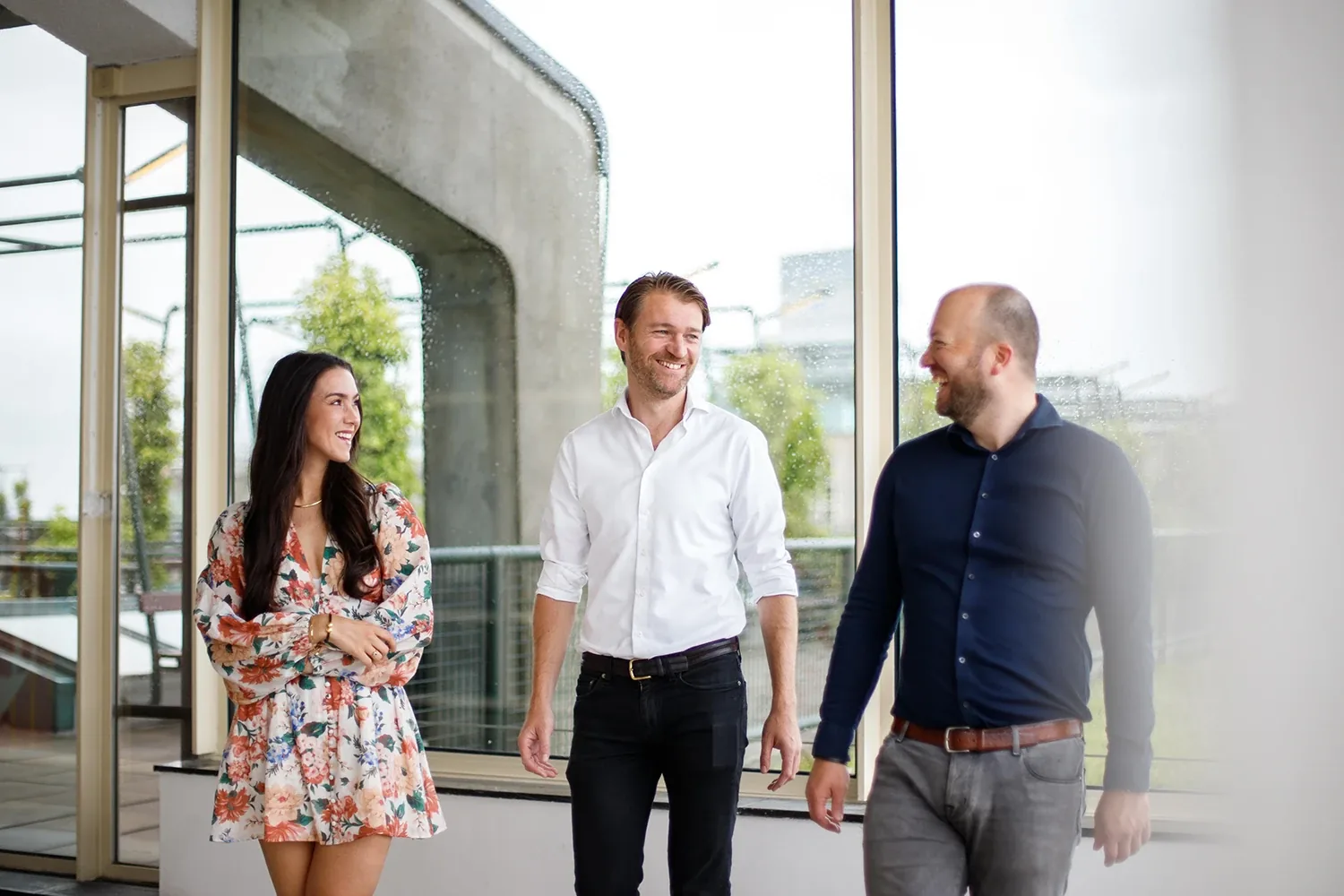 Drie collega's lopen lachend samen door een licht kantoor