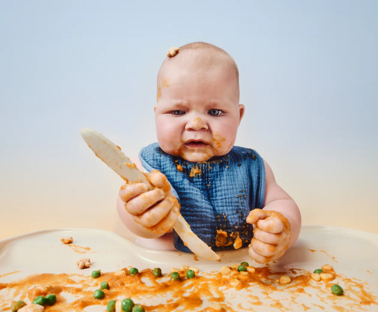 Baby eating at a high chair with a wooden spoon