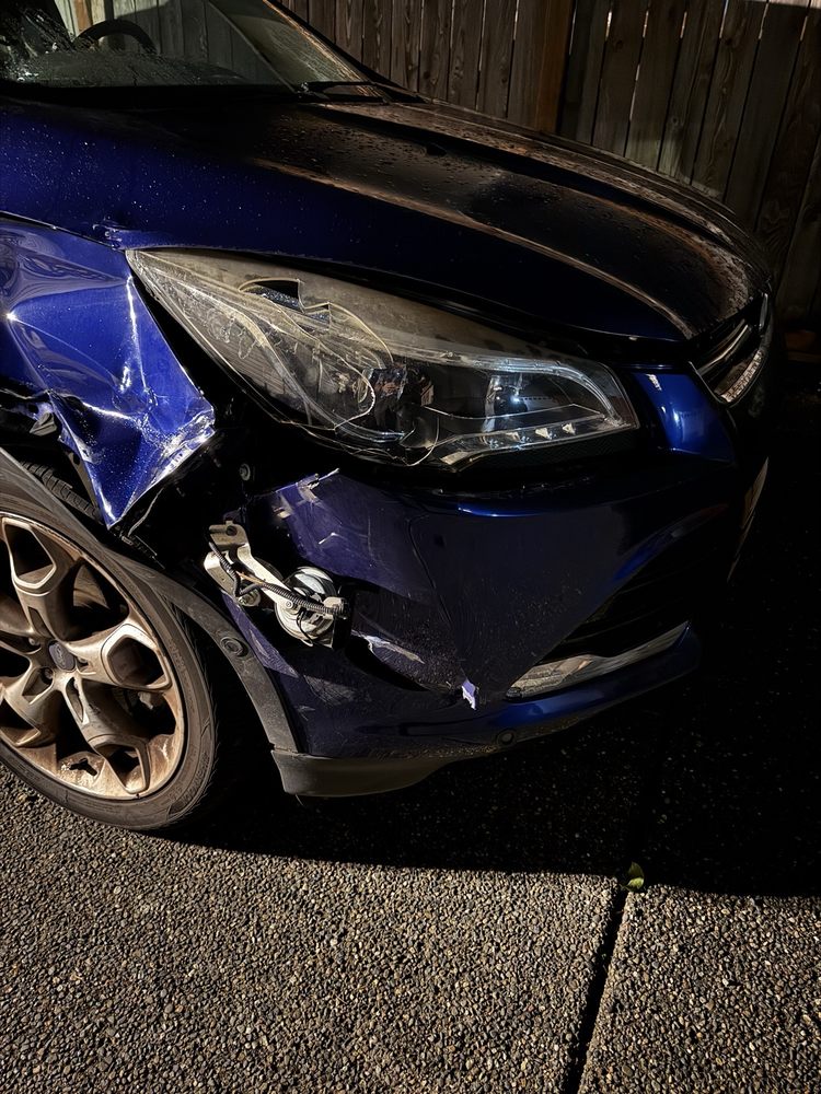 Front corner of a blue Ford Escape as it arrived — crumpled fender, cracked bumper, headlamp taped up