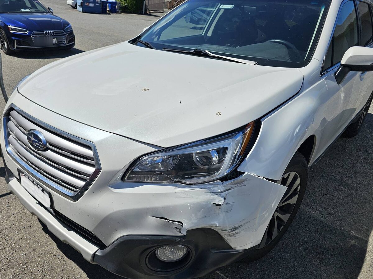 Front of a white Subaru Outback as it arrived, the bumper split and the corner crushed back into the wheel arch