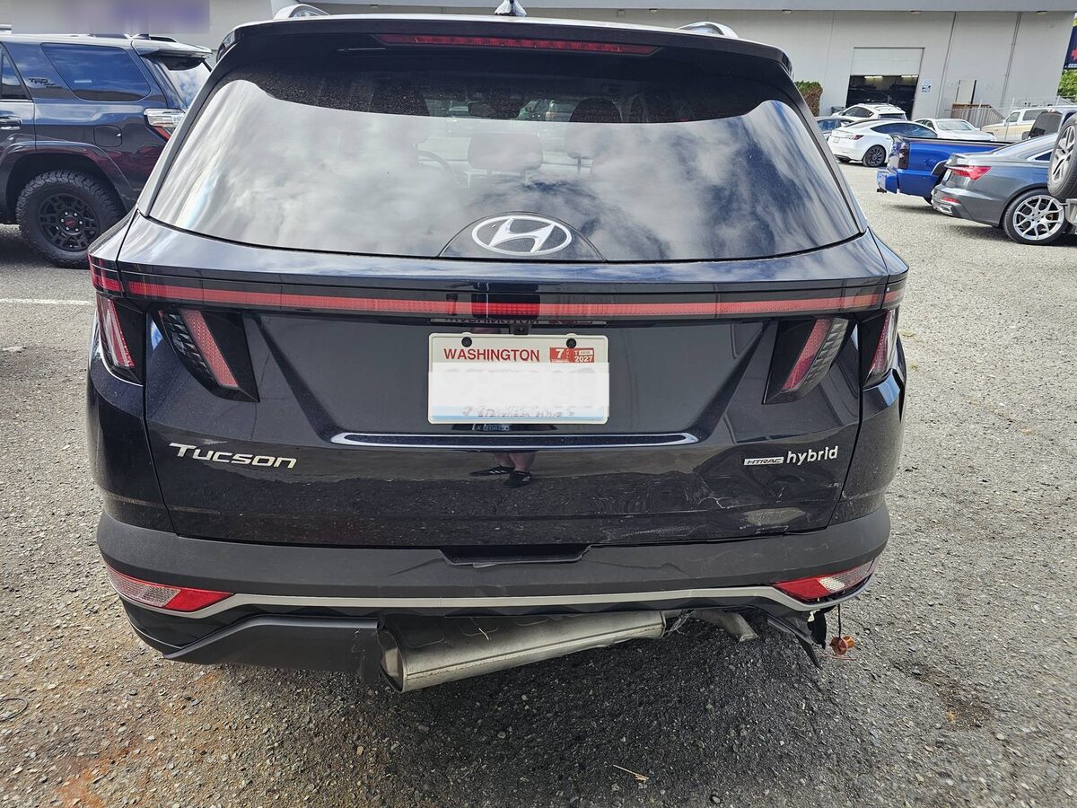 Rear of a black Hyundai Tucson Hybrid as it arrived, the bumper cover hanging off its mounts with the impact bar exposed