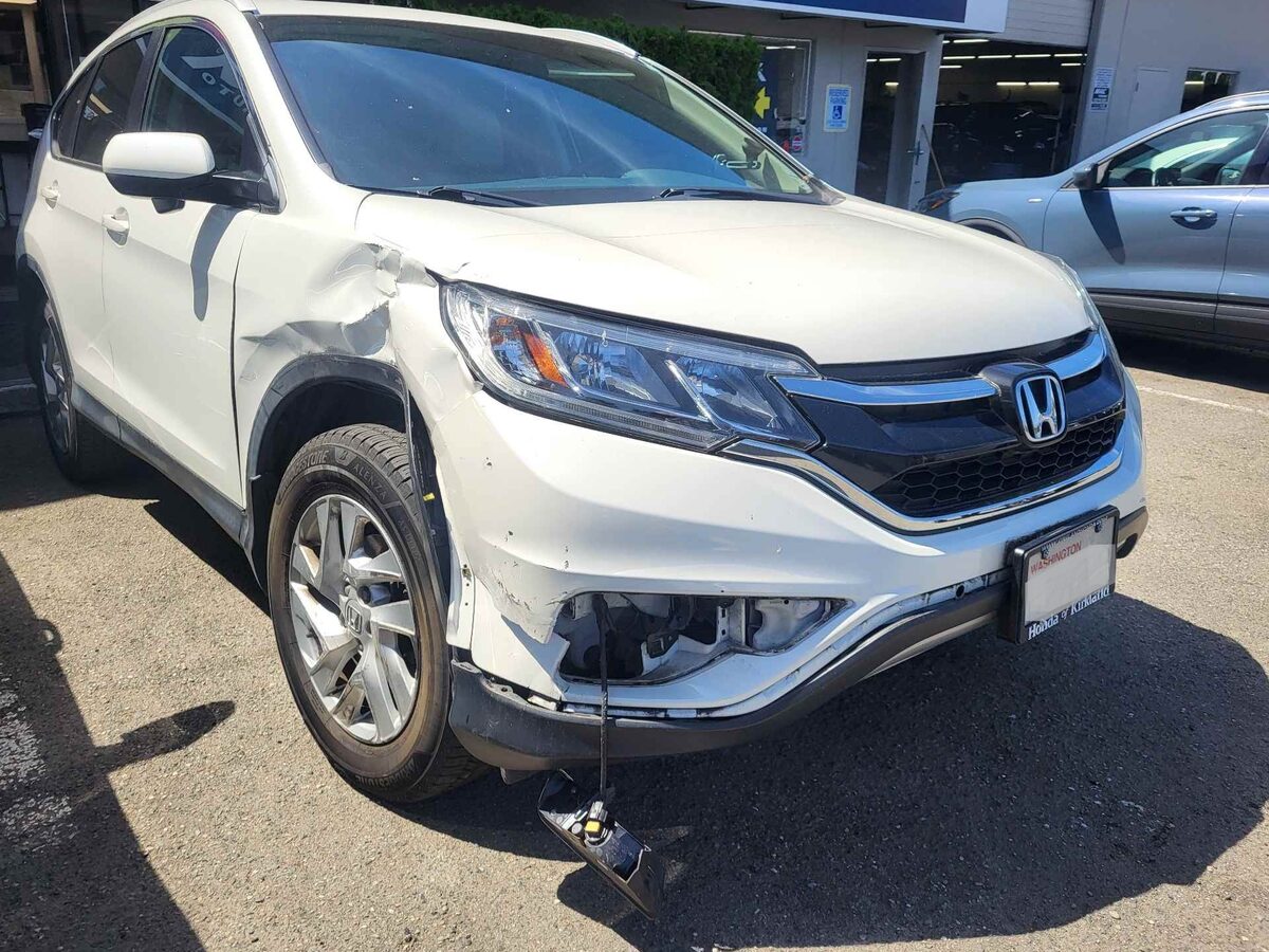 Front of a white Honda CR-V as it arrived, the fender folded into the door and the bumper corner dragged loose