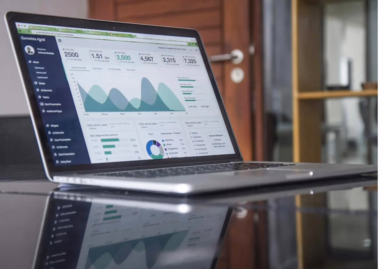 An open laptop on a dark glossy table displaying an analytics dashboard of charts and figures