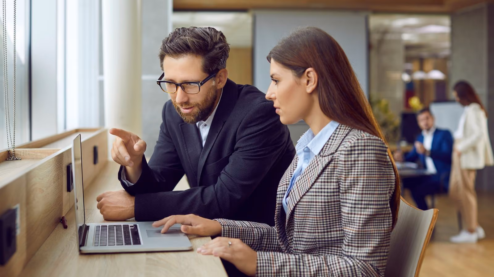 Two executives, one male and one female. The male is providing guidance and advice to the female, who is on her laptop