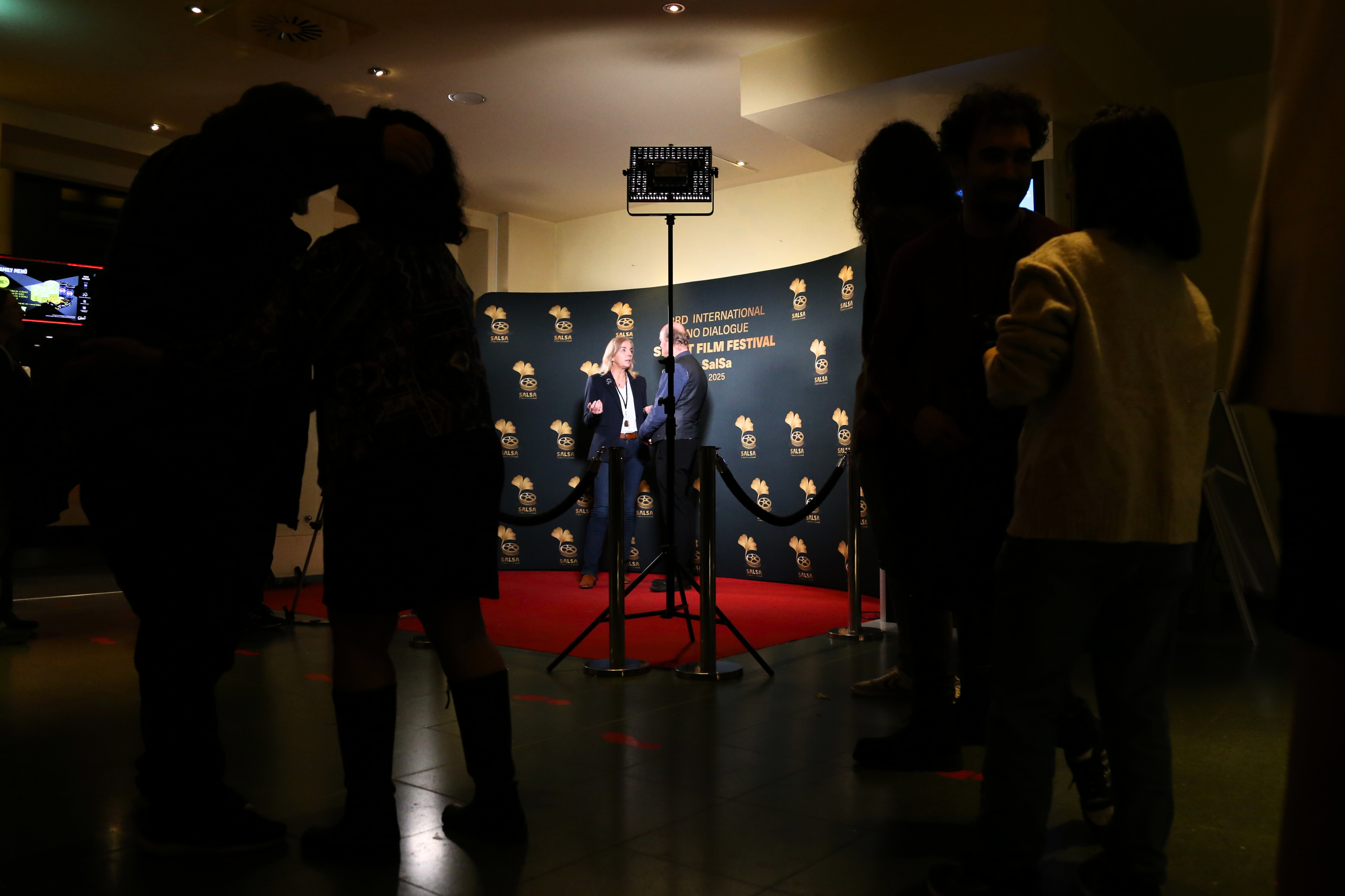 Gäste im dunklen Foyer, im Hintergrund ein Interview auf dem roten Teppich