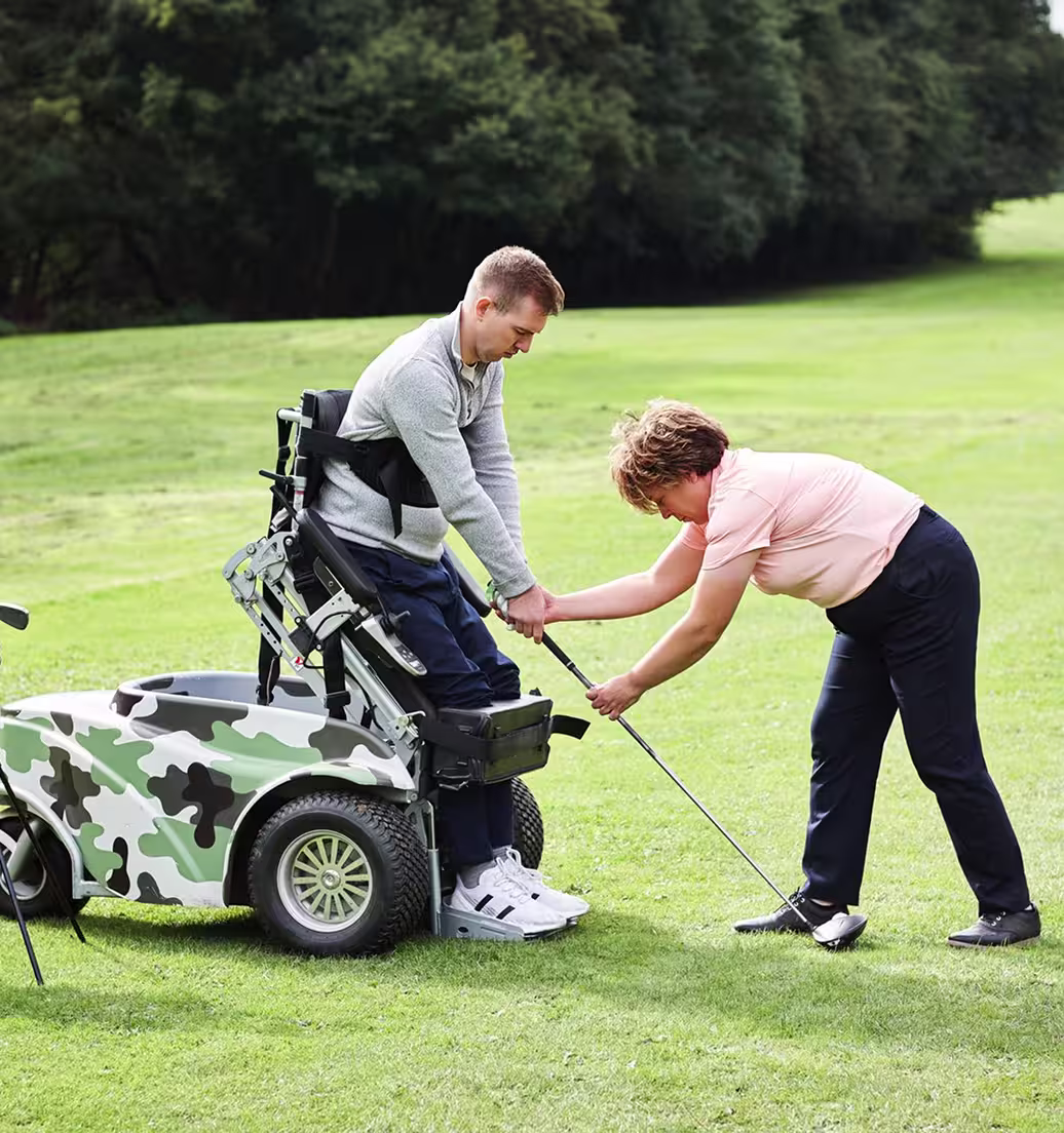 Golf coach assisting a golfer using an adaptive mobility device with their swing on the course