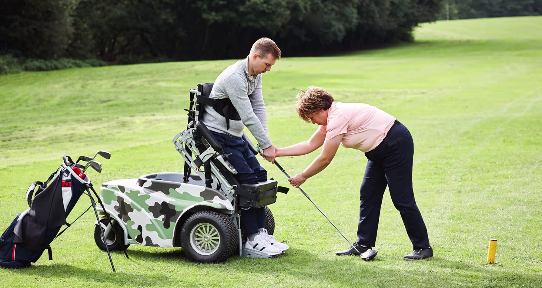 Golf coach assisting a golfer using an adaptive mobility device with their swing on the course