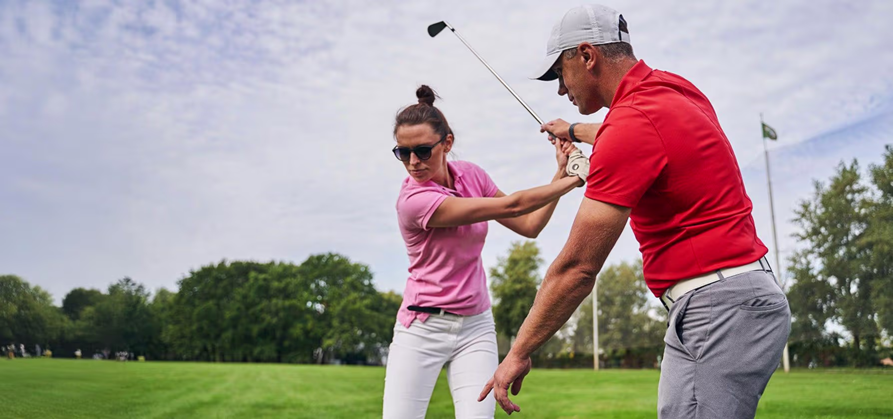 Golf coach adjusting a player's grip during an outdoor skills clinic at sunset