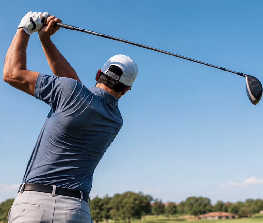 Golfer captured mid-swing at the top of their backswing against a clear blue sky