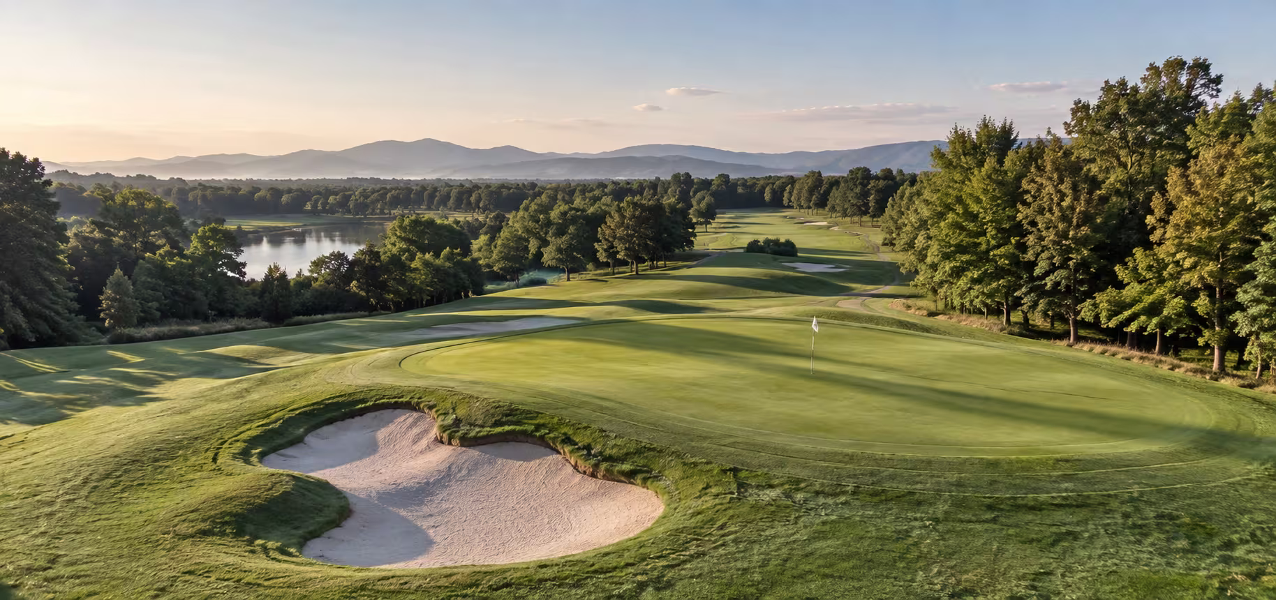 Elevated view of a manicured golf course green surrounded by trees and a bunker