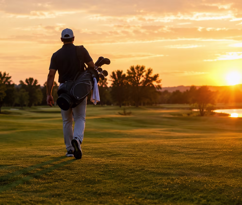 Golfer with a golf bag walking down the fairway at sunset after a lesson