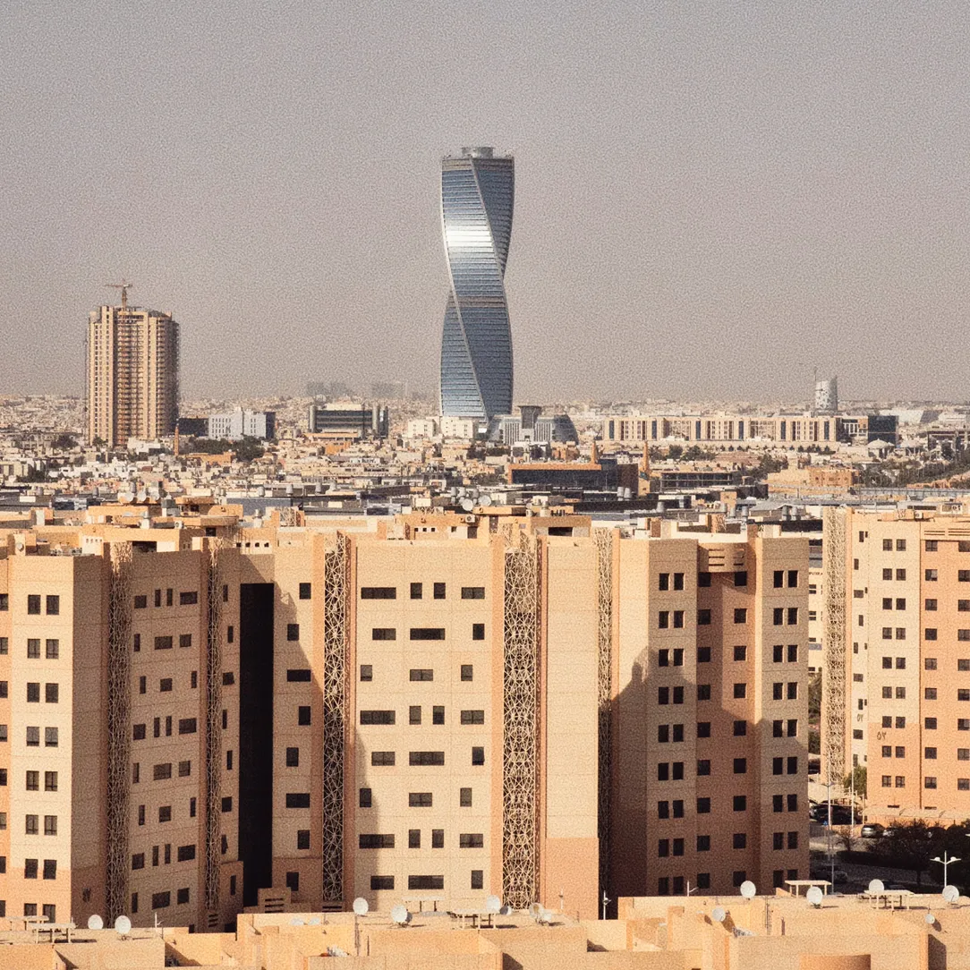 City skyline with beige residential buildings in the foreground and a tall, modern twisted skyscraper in the background under a hazy sky.