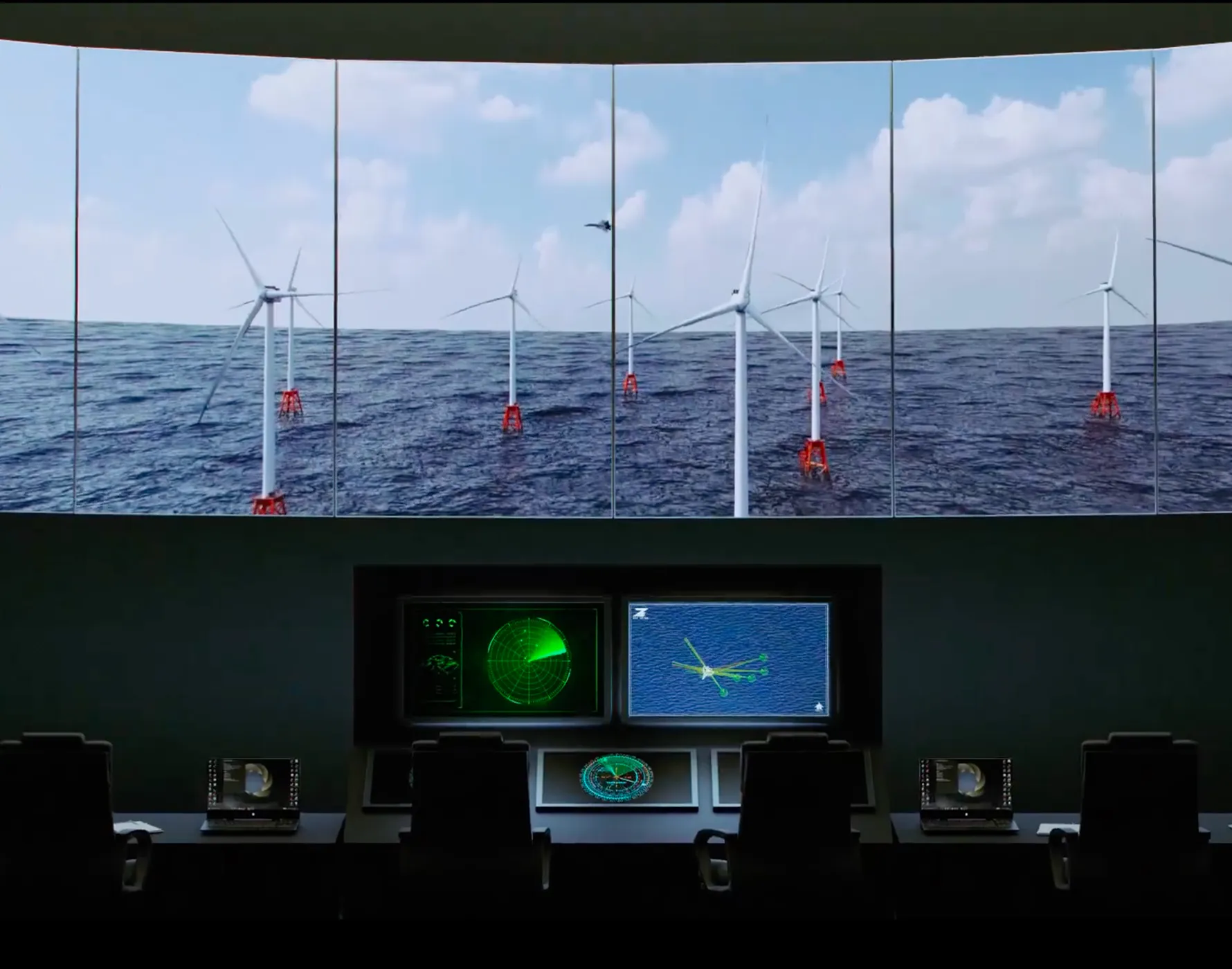 大きなスクリーンに海上の風力発電タービンの遠景が映されている制御室の内部。タービンの基部は赤く、複数の風車が海面から伸びる。制御室の前には複数の椅子とモニターがあり、左側のモニターにはグリーンのレーダー表示、中央右のモニターには海の地図と風車の位置を示すグラフィックが表示されている。