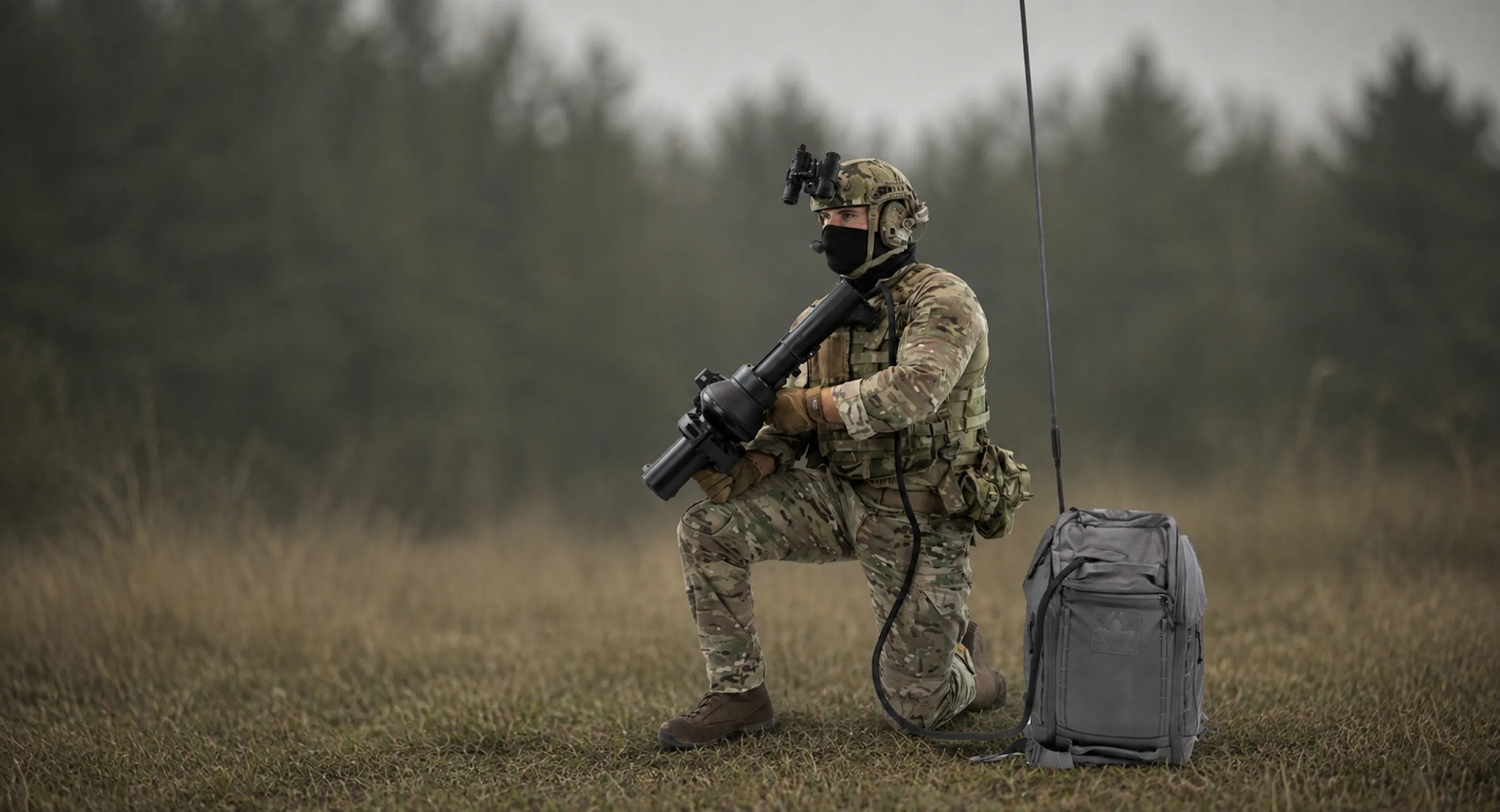 草地にひざまずくカモフラージュ服を着た兵士が、大きな携帯型ミサイル発射装置を構え、背後にアンテナ付きの装備バッグが置かれている。