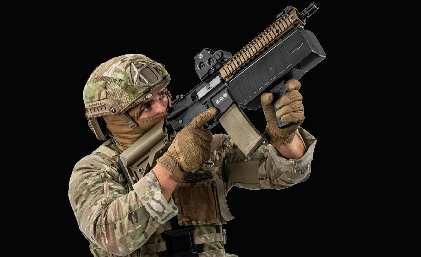 迷彩服とヘルメットを着用し、グローブをはめた兵士が大型の銃を構えて狙っている。