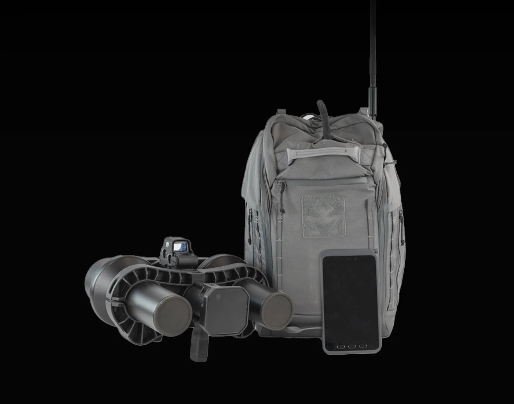 グレーのバックパック、双眼鏡型の夜間戦闘用光学機器、そして黒いスマートフォンが黒い背景に並んでいる。